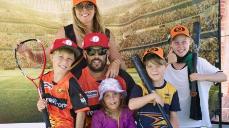 "A Mum and Dad are surrounded by their four children. Everyone is wearing sporting gear with tennis rackets."